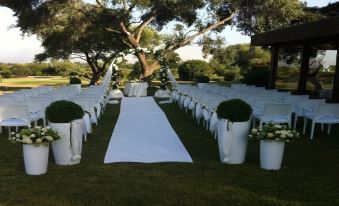a wedding ceremony taking place in a lush green garden , with rows of chairs arranged for guests at Is Molas Resort