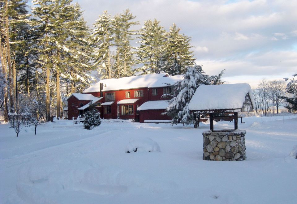 a red house is surrounded by snow - covered trees and a stone well in front of it at Old Saco Inn