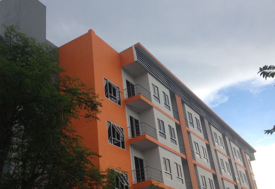 a modern apartment building with an orange and gray exterior , situated under a cloudy sky at V at Panus