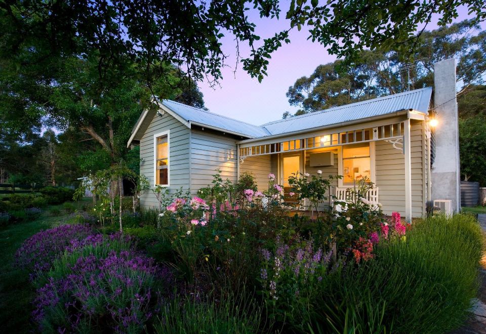 a white house with a porch and a garden filled with flowers and plants , under the light of dusk at The Gums