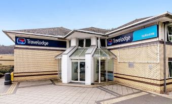 a travelodge hotel with its entrance and exit , featuring a glass door and blue signs above the entrance at Travelodge Stafford M6