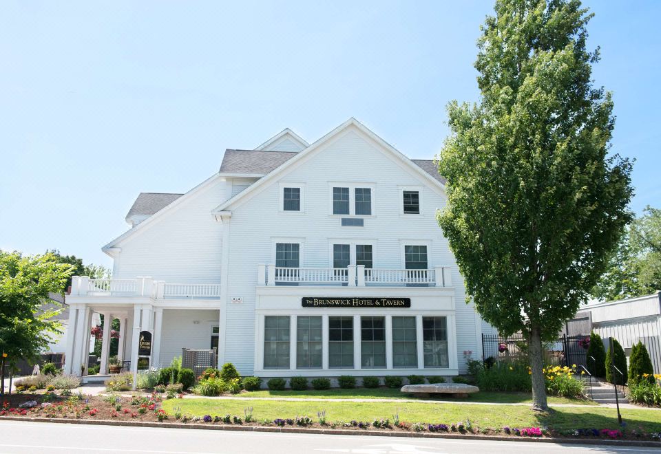 a white building with a sign on the front , located in a residential area near trees and grass at The Brunswick Hotel