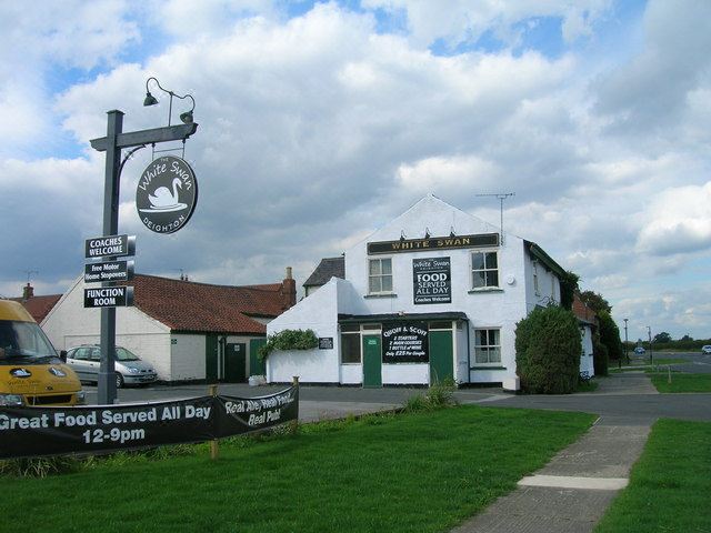 "a large white building with a green roof and the words "" friends served all day 1 2 - 3 0 pm "" on it" at The White Swan Deighton