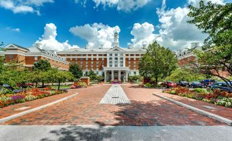 a large brick building with a white clock tower is surrounded by trees and flowers at Hilton Columbus at Easton