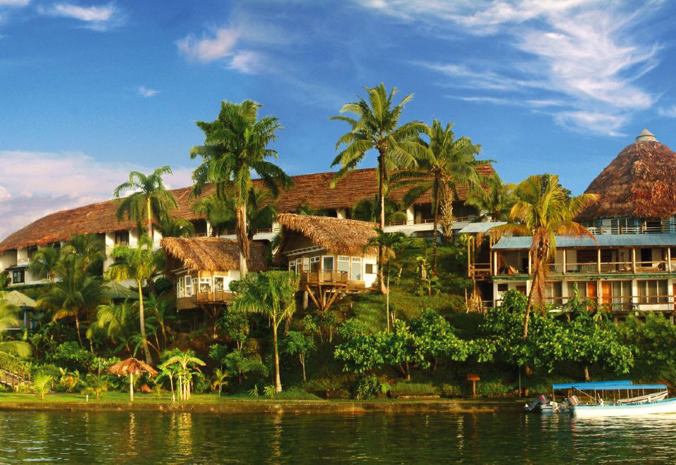 a tropical resort with multiple buildings , palm trees , and a body of water in the background at Villa Caribe