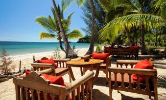 a wooden deck with red cushions and a table , surrounded by palm trees on a beach at VOI Amarina Resort