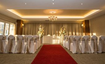 a wedding ceremony taking place in a hotel ballroom , with the bride and groom seated on white chairs at Horsley Lodge