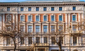 a large , ornate building with multiple windows and balconies , surrounded by trees and under a clear blue sky at Hotel Moments Budapest