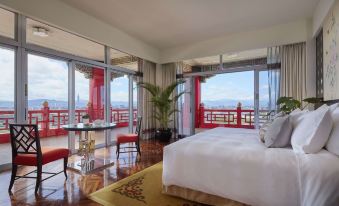 The bedroom features large windows and a balcony that overlook the city, with an elegant bed positioned in front at The Grand Hotel