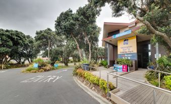 a modern building with a yellow roof , surrounded by trees and grass , and a winding road leading to the entrance at Wellington Top 10 Holiday Park