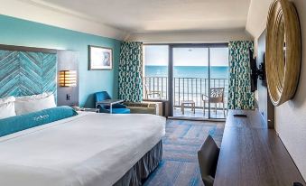 a bedroom with a bed , desk , and sliding glass door leading to a balcony overlooking the ocean at Crystal Coast Oceanfront Hotel
