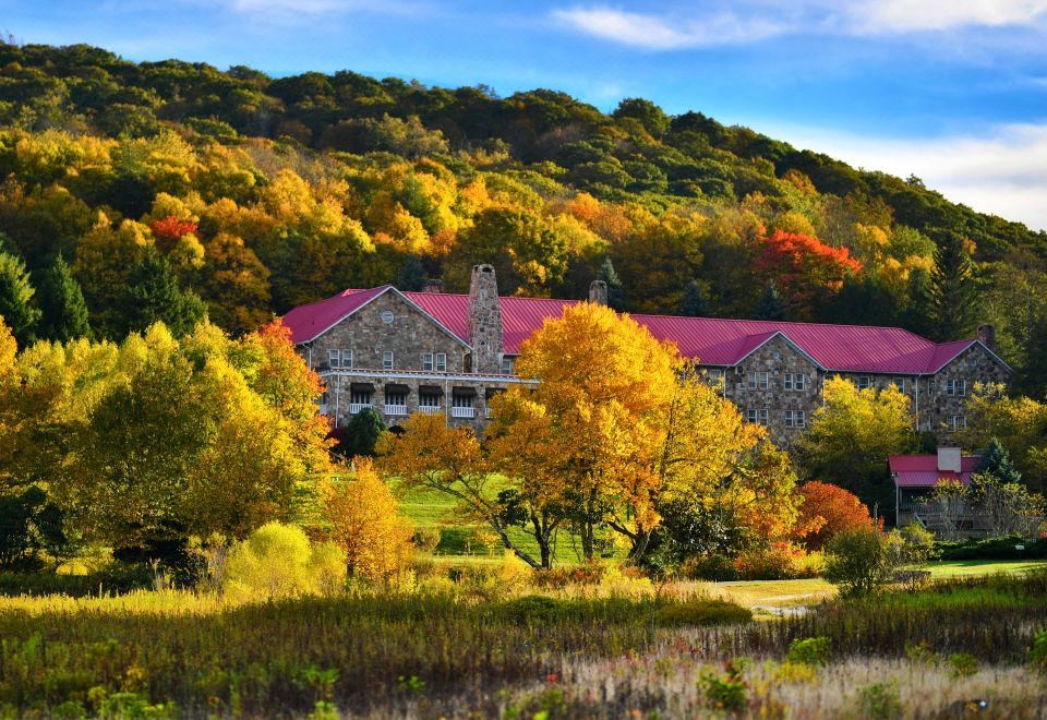 a large stone building with a red roof is surrounded by trees and hills in the autumn season at Mountain Lake Lodge