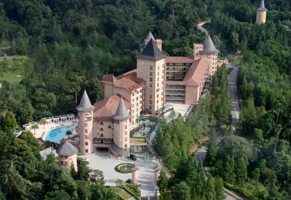 aerial view of a large , pink castle - like building surrounded by lush greenery and a pool at The Chateau Spa & Wellness Resort