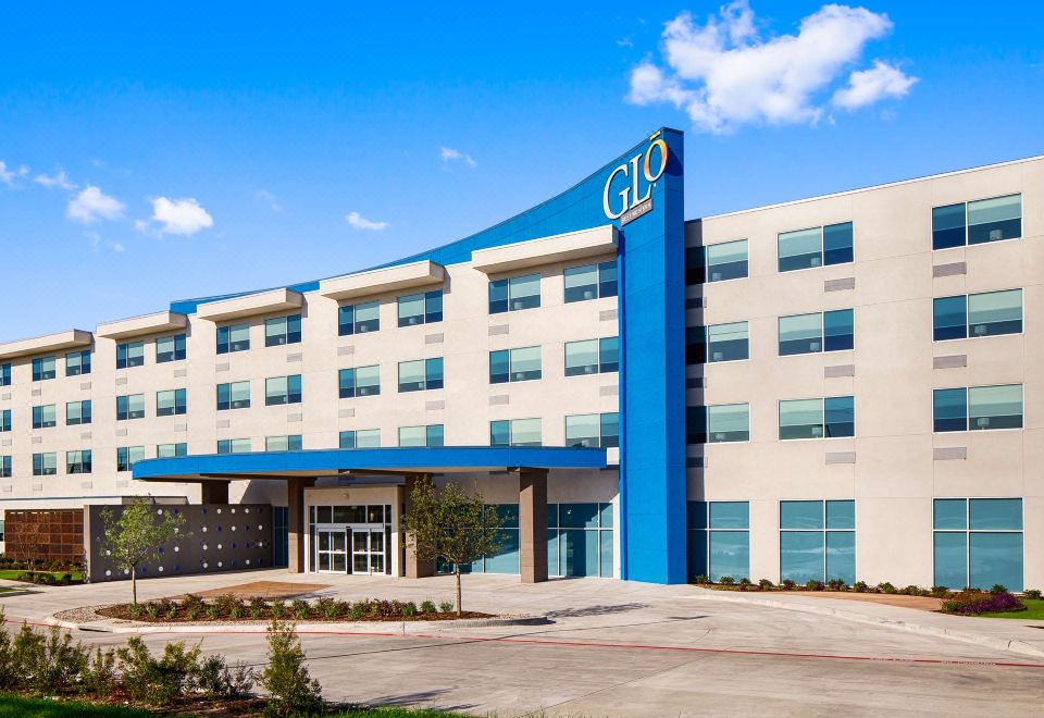 a large , modern hotel with a blue and white exterior , situated in a parking lot at GLo Best Western DeSoto Dallas