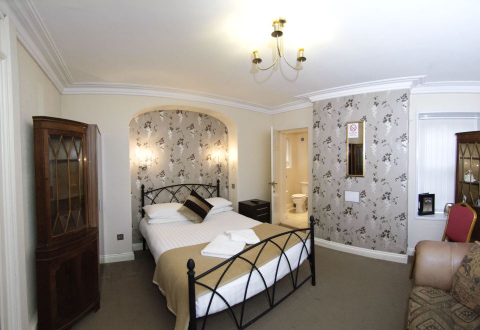 a large bed with a black metal frame is in the middle of a room with floral wallpaper at The Old Rectory