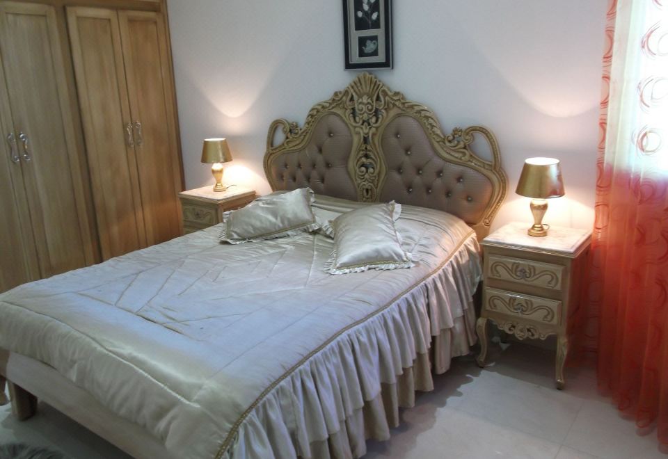 a luxurious bedroom with a large bed , gold headboard , and matching nightstands , set against a white wall at Rahma