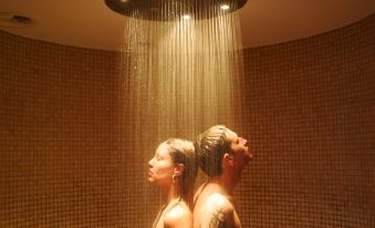 a man and a woman are standing in a shower , looking at each other with serious expressions at Hotel Sonnenblick