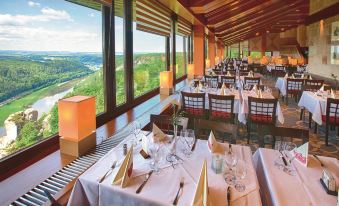 a restaurant with multiple dining tables and chairs , all set for a meal , overlooking a scenic view at Berghotel Bastei