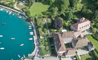 aerial view of a large mansion surrounded by water , with boats docked in the bay at Abbaye de Talloires