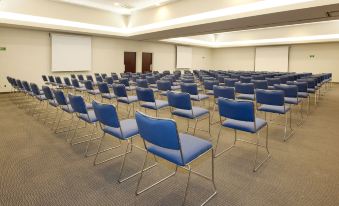 a conference room with rows of blue chairs and a large screen at the front at City Express by Marriott Nogales