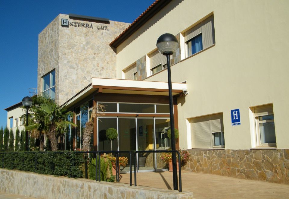 a modern building with a stone facade , large windows , and a glass entrance , surrounded by trees and a clear blue sky at Hotel Sierra Luz