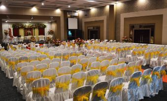 a large banquet hall with numerous white and yellow chairs arranged in rows , ready for an event at Pematang Siantar