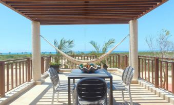 a dining table with chairs is set up on a patio overlooking the ocean , with a hammock hanging from the ceiling at Villas Grand Marina Kinuh