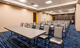 a conference room with rows of tables and chairs , a blue carpeted floor , and large windows at GLo Best Western DeSoto Dallas