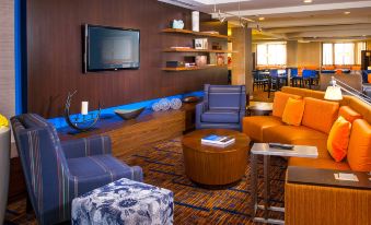 a modern living room with blue and orange furniture , a large screen tv , and a wooden shelf at Courtyard Richmond Northwest/Short Pump