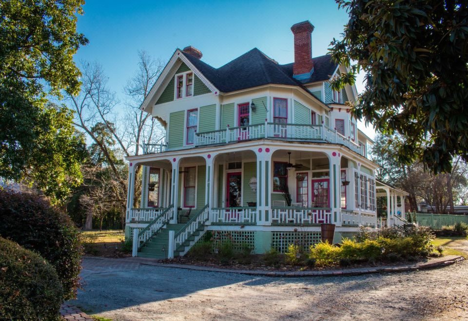 a large , two - story victorian - style house with a red roof and green trim , situated in a wooded area at Peacock Place