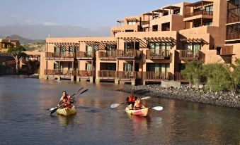 two people are canoeing on a river in front of an apartment building with many windows at Barceló Tenerife