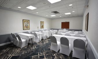 a large conference room with white tables and chairs , a television on the wall , and paintings on the walls at Holiday Inn Hazlet