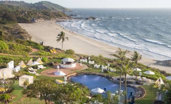 a beach scene with a large pool surrounded by lounge chairs and umbrellas , as well as a sandy shore and palm trees at W Goa