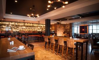 a modern restaurant with wooden tables , chairs , and a bar area , surrounded by bar stools and a brick wall at Oriel House Hotel
