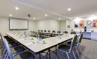 a conference room with several rows of chairs arranged in a semicircle , and a projector mounted on the wall at Ibis Styles Canberra Tall Trees