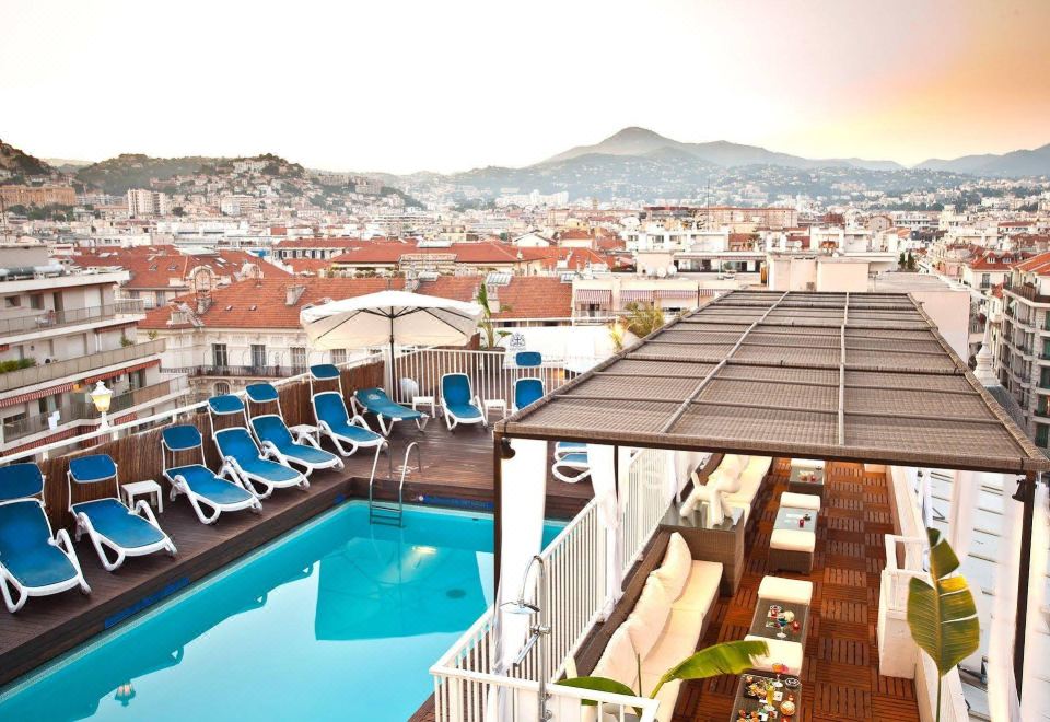 a rooftop pool surrounded by chairs and umbrellas , with a city view in the background at Splendid Hotel & Spa Nice