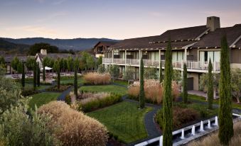 a large building surrounded by a lush green garden , with tall trees and bushes in the background at Rosewood Sand Hill