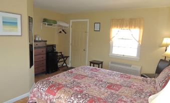 a bedroom with a bed , dresser , and chair , featuring yellow walls and a window with curtains at The Clipper Inn