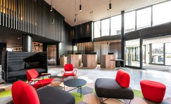 a modern , well - lit hotel lobby with red and black chairs , couches , and tables arranged in an open space at Radisson Hotel Zurich Airport