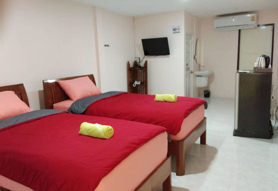 a hotel room with two beds , each topped with red sheets and towels , and a bathroom with a toilet at Smile Resort
