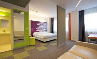 a modern hotel room with a large bed , couch , and various furnishings , including curtains and a mirror at Mercure Milano Agrate Brianza