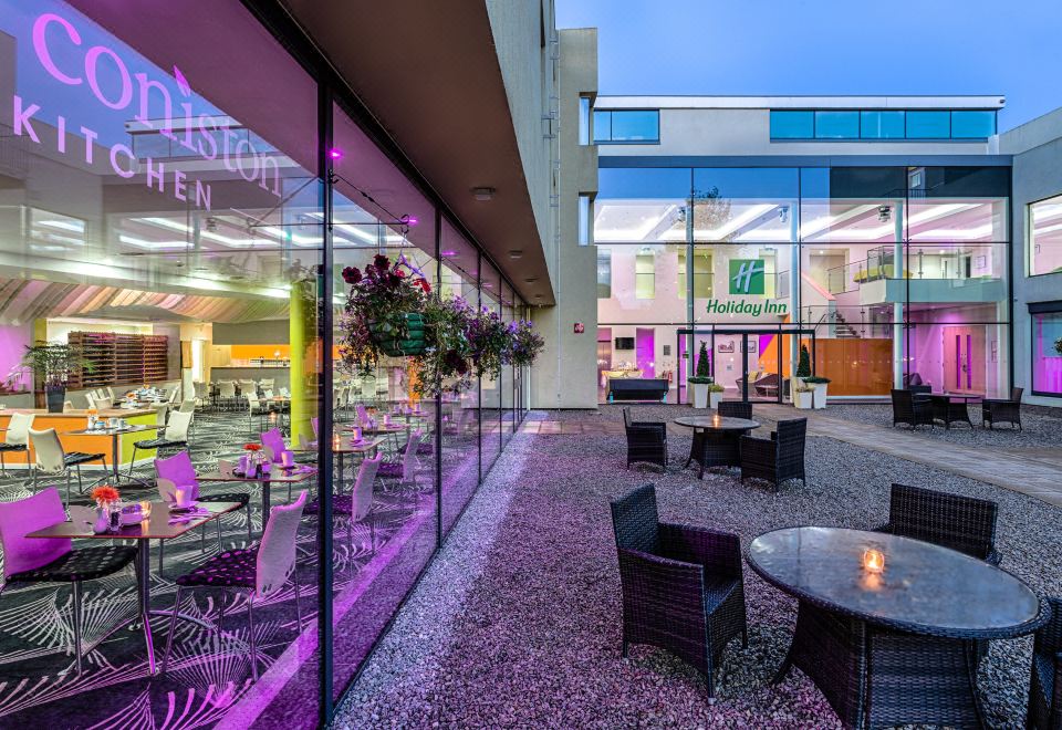 a large building with a glass door and windows , as well as several tables and chairs outside the building at Holiday Inn Sittingbourne