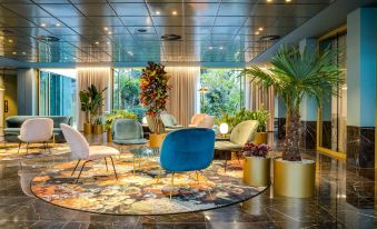 a modern , well - lit living room with multiple chairs and couches arranged around a large window at NH Collection Antwerp Centre