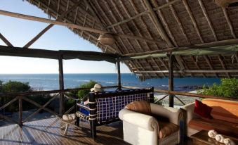 a room with a couch , chairs , and a view of the ocean through a thatched roof at Lazy Lagoon