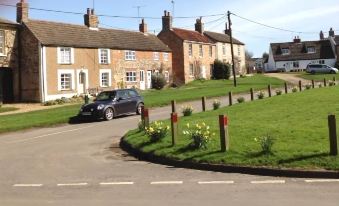 a car is parked on a street with houses and greenery in the background , under a clear blue sky at Chalk and Cheese