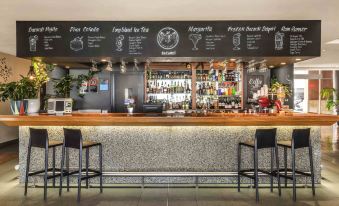 a modern bar with a long counter and black chairs , featuring a menu board on the wall at Ibis Sydney Darling Harbour