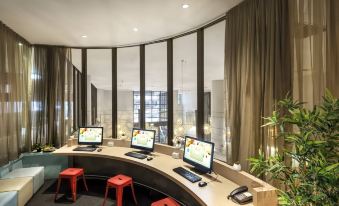 a computer lab with three monitors , three red stools , and a window view of a cityscape at Ibis Melbourne Hotel and Apartments