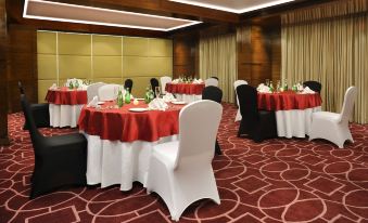 a dining room with several round tables covered in red tablecloths and surrounded by white chairs at Four Points by Sheraton Ahmedabad