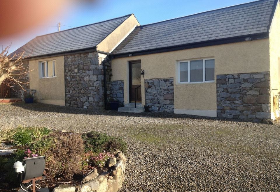 a house with a stone facade and blue roof is shown in the foreground , while the sky is clear at Brigadoon