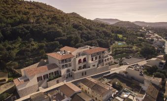 aerial view of a large white building surrounded by trees and mountains , with a pool in the foreground at Hotel Creu de Tau Art&Spa-Adults Only